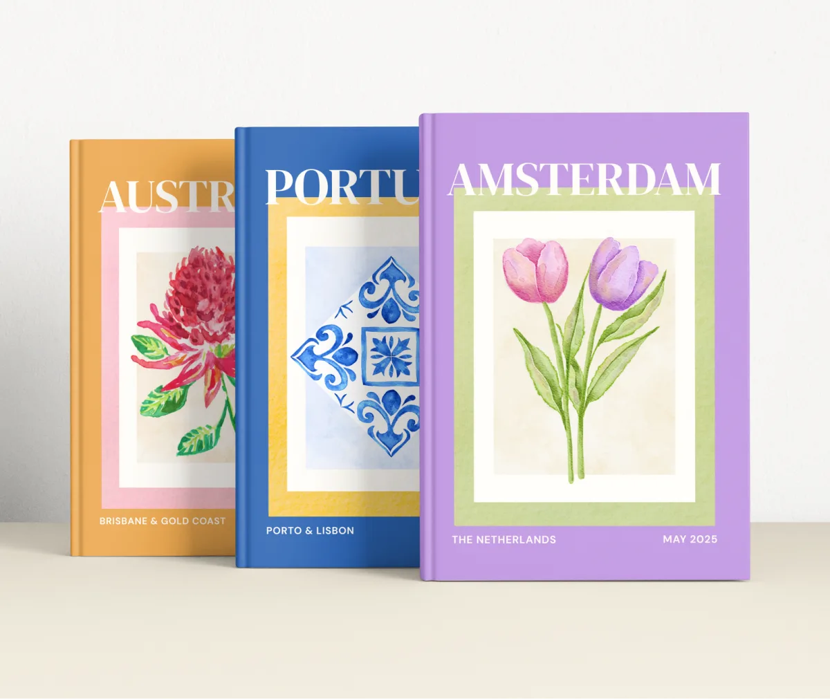 Australia, Portugal and Amsterdam travel photobooks standing side by side, each with a watercolour motif on a matte hardcover